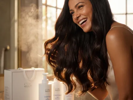 Mulher rindo, cabelo longo em luz de janela, com a linha Absolute Haircare ao lado.